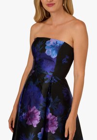 Bezramienna sukienka w kwiaty z czarnego satyny, z dużymi fioletowymi i niebieskimi kwiatami, usztywnioną górą oraz rozkloszowaną spódnicą z plisami.