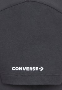 Temno siva kapuca iz mešanice bombaža; ima bel logo "CONVERSE" na dnu z zvezdnim dodatkom in šivom na stranskem šivu.