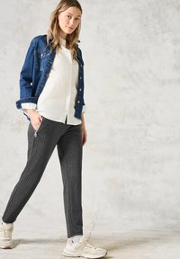 Veste en denim, chemise blanche à boutons, pantalon gris à rayures, et baskets claires. Tenue décontractée avec des textures et des couleurs variées.