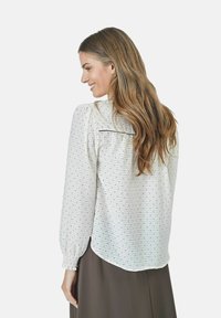 White blouse with black polka dots, long sleeves with gathered cuffs, and a relaxed fit. Features a back yoke with subtle gathering detail.