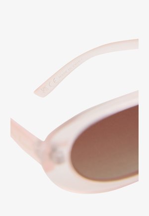 Růžové průhledné obroučky brýlí zobrazující text „UKCA CE Made in China“ a částečně viditelné hnědě tónované oválné čočky.