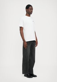 Hvit bomulls t-skjorte med korte ermer, kombinert med løstsittende svarte denimjeans med sidessøm. Svart fottøy fullfører antrekket.