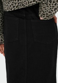 Falda de mezclilla negra con dos bolsillos traseros, diseño ajustado y costuras visibles a lo largo de las costuras, con un aspecto de tela texturizada.