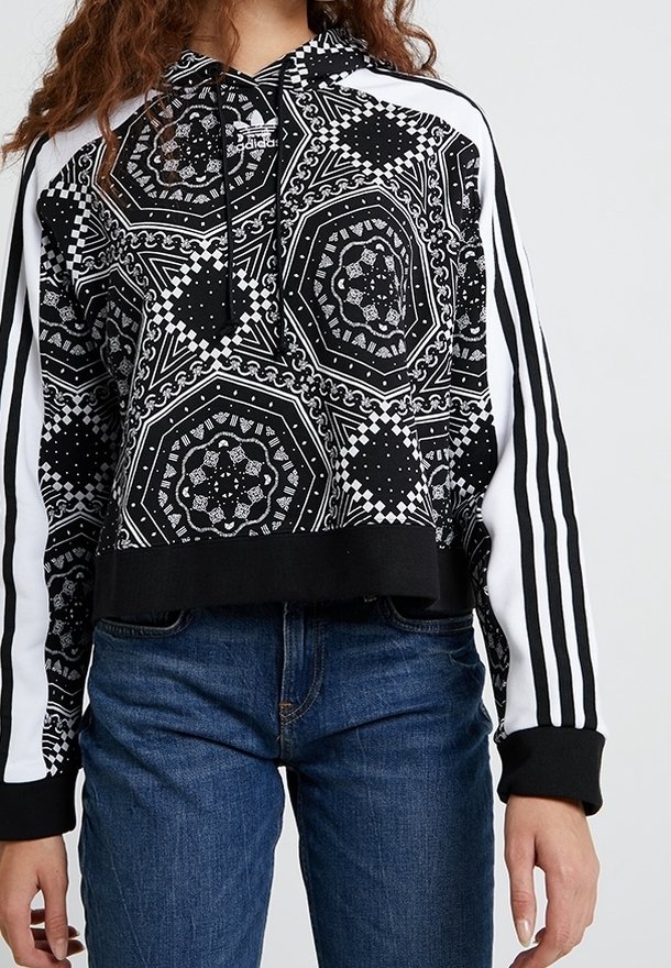 Oříznutá černobílá mikina s geometrickými vzory, kapucí se stažícím šňůrkem a bílými pruhy po stranách na černých rukávech.