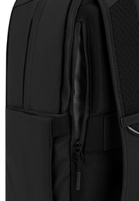 Mochila negra con un exterior suave y texturizado, un compartimento con cremallera y un panel de malla para ventilación. Diseño minimalista y detalles.