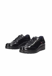 Zapatos negros brillantes con puntera redondeada, diseño con cordones y suela gruesa y texturizada. Logos notables cerca del talón. Material sintético suave.