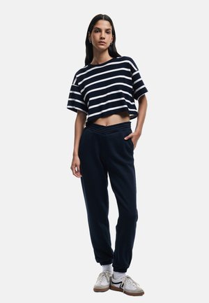 Marine-stribet cropped t-shirt med løstsiddende pasform, kombineret med marine jogger-bukser med elastisk talje og manchetter. Båret med hvide sneakers.