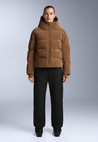Hnědá péřová bunda s vysokým límcem, se zipovým zapínáním a horizontálním prošíváním. V kombinaci s černými kalhotami a černou obuví.