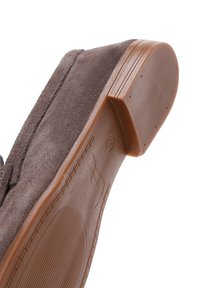 Chaussure en suède marron à enfiler avec une semelle en caoutchouc texturée et basse. La semelle présente des motifs circulaires et des lignes pour une meilleure adhérence. Design simple et fonctionnel.