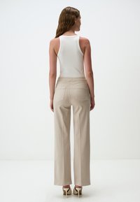 Pantaloni beige a gamba larga con una texture liscia, abbinati a un top bianco aderente. L'outfit presenta un design pulito e tasche posteriori discrete.