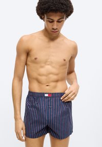 Μπλε βαμβακερά μποξεράκια με κάθετες κόκκινες ρίγες, ελαστική μέση και κλείσιμο με κουμπί μπροστά. Απλή υφή και casual σχέδιο.