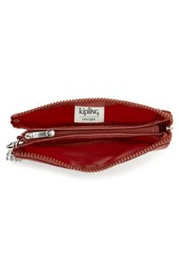 Billetera Kipling roja con cierre de cremallera, que cuenta con dos compartimentos forrados en tela suave y un borde exterior texturizado. Acentos de hardware plateado.