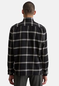 Chemise à carreaux noirs avec des lignes blanches, manches longues, col boutonné et coupe décontractée. Présente une légère texture et des poignets à boutons.