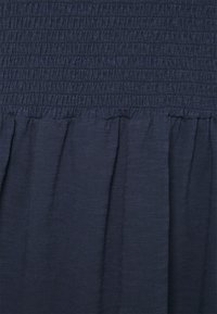 Granatowa sukienka z marszczonym gorsetem, teksturowym materiałem i zwiewnym dołem. Górna część ma zebrane szwy dla dodatkowego wykończenia.