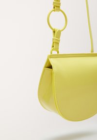 Borsa in pelle gialla con forma curvata e strutturata, caratterizzata da un accento hardware rotondo sulla tracolla regolabile e una superficie liscia.