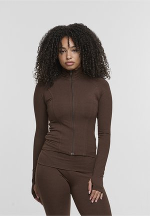 Brązowa sportowa kurtka zapinana na zamek z wysokim kołnierzem, długimi rękawami i otworami na kciuki, wykonana z lekkiego, elastycznego materiału.