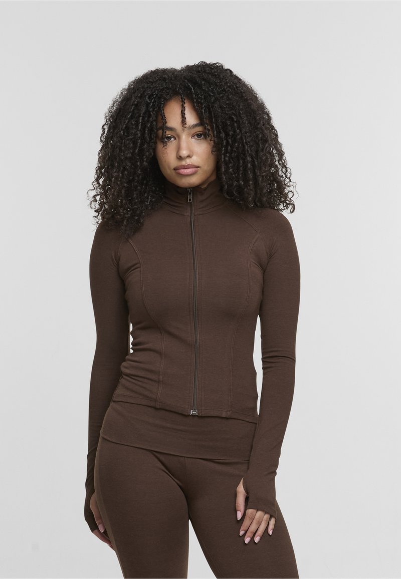 Veste de sport marron à fermeture éclair, avec un col montant, des manches longues et des passages pour les pouces, fabriquée dans un matériau léger et extensible.