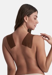 Nastro adesivo marrone applicato su pelle nuda, con una consistenza morbida e forma rettangolare, con un aspetto liscio e senza soluzione di continuità.