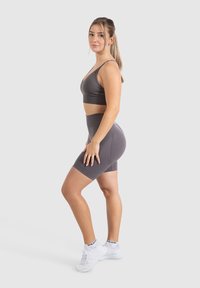 Grahamathletikset mit einem enganliegenden Sport-BH und hoch taillierten Shorts, aus glattem, dehnbarem Stoff, getragen mit weißen Sportschuhen.