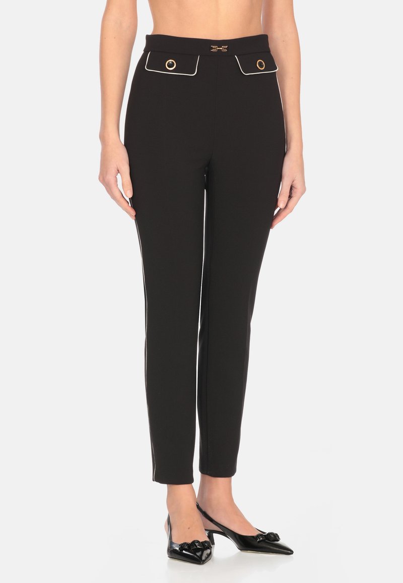 Pantaloni neri aderenti con vita alta, due tasche frontali, dettagli in bottone dorato e piping bianco lungo i lati. Tessuto dalla texture liscia.