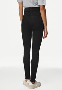 Jeans skinny de talle alto en denim elástico, con bolsillos traseros detallados y un ajuste elegante, combinados con zapatillas ligeras.