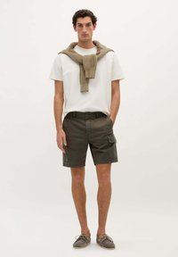 Shorts cargo khaki cu multiple buzunare, asortați cu un tricou alb și un pulover din tricot aruncat pe umeri. Încălțăminte casual inclusă.
