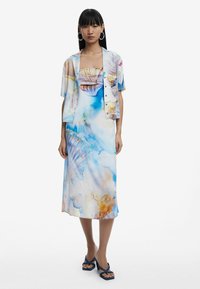Lange, voolav sinine ja valge maxi kleit abstraktsete mustritega, koos lühikeste varrukatega mustrilise jakk. Sinised rihmadega sandaalid täiendavad välimust.