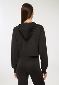 Hoodie cropped nera con cappuccio, maniche lunghe e polsini a costine. Tessuto liscio con un design semplice e senza loghi o fantasie visibili.