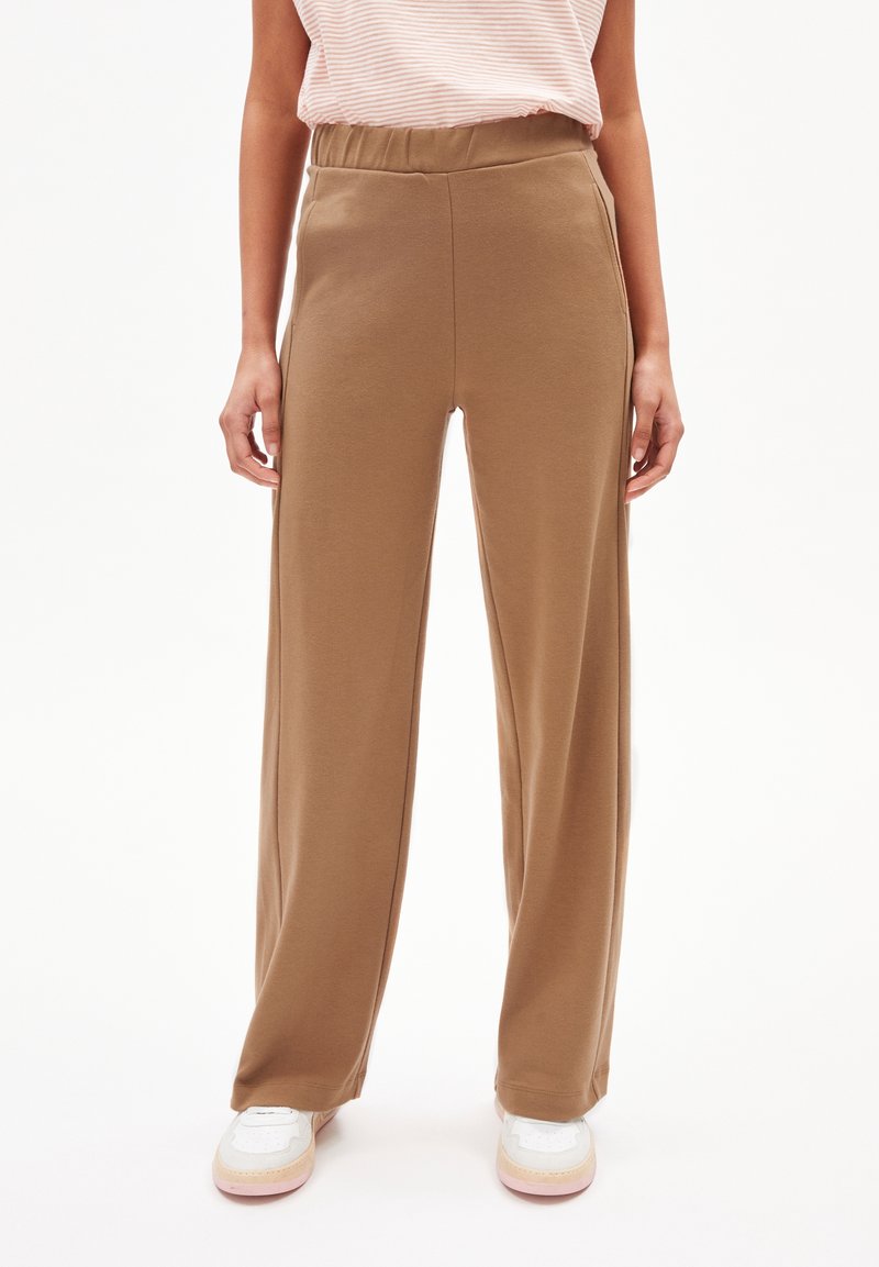 Pantalons large marron avec une taille élastique, en tissu doux, associés à des baskets blanches et un top rayé clair.