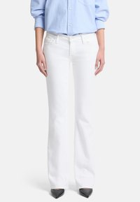 Jeans bianchi a gamba svasata in denim, con vita media, cinque tasche e finitura pulita, abbinati a una camicia azzurra a bottoni.