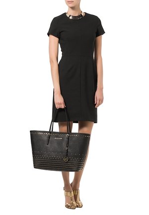 Sort tote bag med nitter, blødt lædermateriale og lange håndtag. Bærer en kort sort kjole og guldfarvede sko.