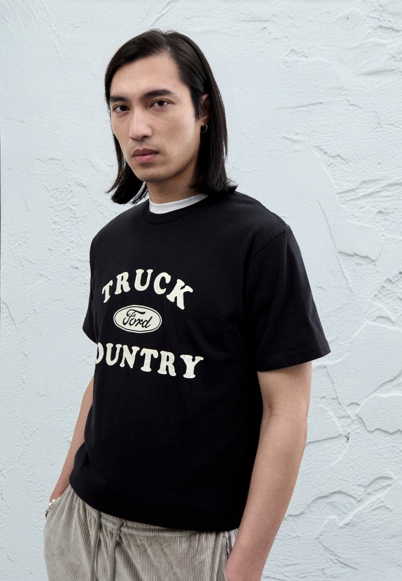 Juodas medvilninis marškinėlis su baltu užrašu „TRUCK“ ir „COUNTRY“ bei Ford logotipu. Lygus audinys, apvalus kaklas, trumpomis rankovėmis.