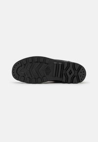 Black rubber shoe sole with a textured tread pattern, featuring grooves and raised sections for traction and stability.