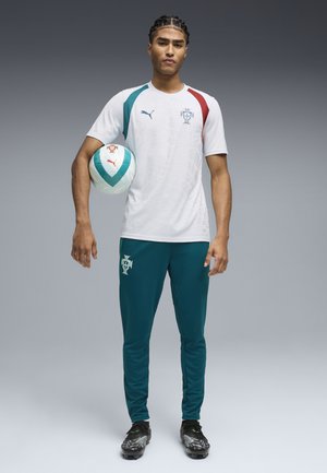 Ung mand i Portugal fodboldtrøje, der holder en fodbold ved siden, står på en grå gradient baggrund.