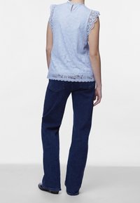 Haut en dentelle bleu clair avec manches courtes à volants, ourlet festonné et détail dos en trou de serrure, associé à un jean denim bleu foncé.