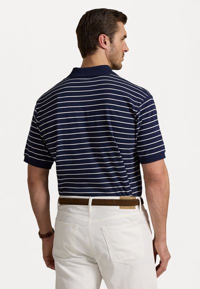 Granatowa i biała polo w paski z kołnierzykiem, krótkimi rękawami i luźnym krojem, zestawiona z białymi spodniami i brązowym paskiem.