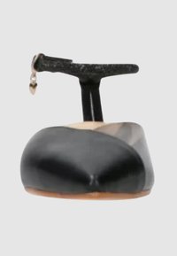 Scarpa piatta in vernice nera con punta affusolata. Presenta una sottile cintura nera con un charm a forma di cuore. Texture liscia, design minimale.