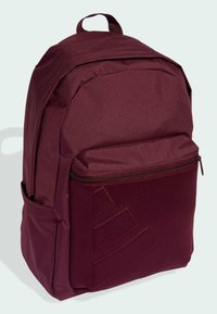 Zaino bordeaux in tessuto testurizzato con finitura liscia, dotato di tasca frontale con zip e tasca laterale in rete. Dettaglio di design discreto in rilievo.