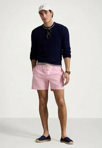 Lekkie różowe szorty kąpielowe ze sznurkiem, połączone z granatowym swetrem w splot warkoczowy, granatowymi espadrylami i białą czapką. Casualowy strój.