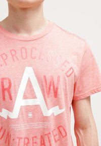 Różowa melanżowa koszulka z krótkim rękawem, z dużą białą grafiką i napisem "RAW". Wykonana z miękkiej, lekkiej bawełny.