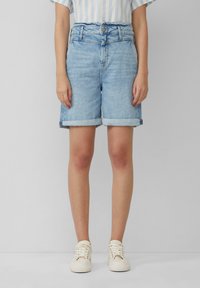 Jasnoniebieskie szorty dżinsowe z wysokim stanem, z podwiniętym dołem i zapięciem na guziki z przodu. Uzupełnione białymi trampkami.