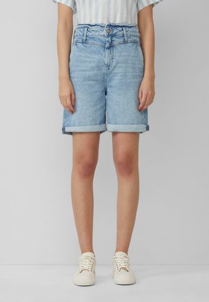 Shorts en denim bleu clair, avec une taille haute, un ourlet retroussé et une fermeture à bouton sur le devant. Associés à des baskets blanches.