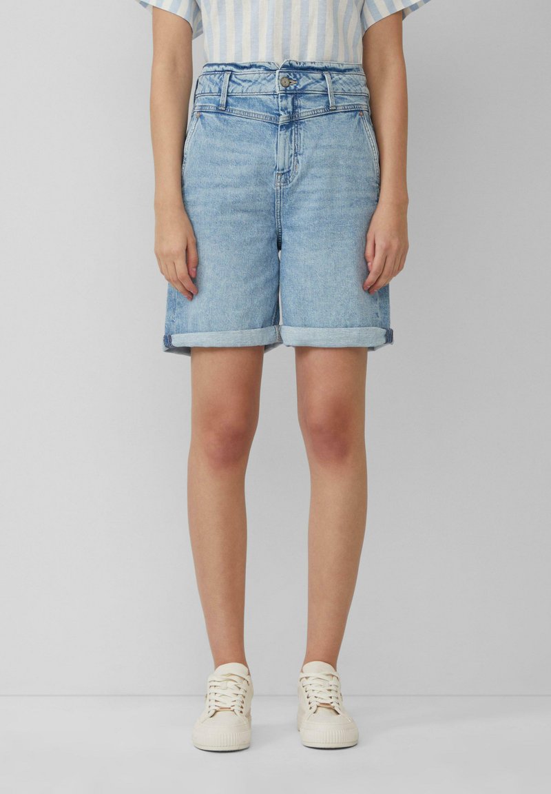 Jasnoniebieskie szorty dżinsowe z wysokim stanem, z podwiniętym dołem i zapięciem na guziki z przodu. Uzupełnione białymi trampkami.