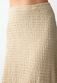 Beige, strukturierter Rock mit einem gerafften Design. Das Material hat ein zerknittertes Aussehen, das ein wellenförmiges Muster im gesamten Stoff erzeugt.