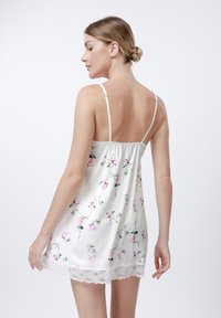 Camisón blanco con flores rosas y hojas verdes, dobladillo de encaje y tirantes ajustables finos, con una textura suave similar al satén.