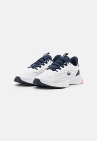 Chaussures de sport blanches avec accents bleu marine, empeigne en maille pour la respirabilité, semelle texturée et marquage visible sur le côté et la languette.