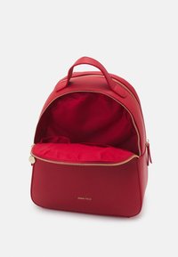 Sac à dos rouge en cuir synthétique lisse, avec une fermeture éclair dorée, une forme arrondie et un intérieur spacieux doublé de tissu.