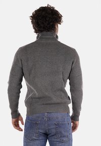 Maglione grigio a coste con colletto alto, realizzato in materiale di maglia spesso. Indossato con jeans in denim blu, che mettono in mostra un design aderente e un tessuto strutturato.
