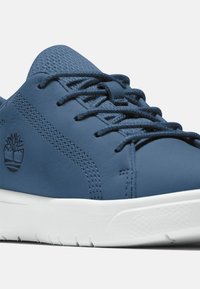 Zapatillas de cuero azul con acentos texturizados, cordones planos y suela blanca. Logotipo distintivo en el costado con detalle de costura en contraste.