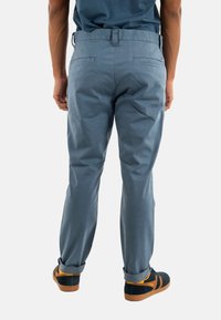 Pantalones de algodón azul claro con un diseño de pierna recta, que cuentan con una cintura con pasadores para cinturón y dobladillo acampanado, combinados con zapatos oscuros.